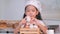 An Asian little girl wearing a white chef hat is sitting play and talking to eggs in a wooden basket in the kitchen