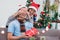 Asian lovers couple, girlfriend surprise boyfriend by giving Christmas present at sofa with xmas decoration tree at house