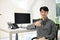 Asian male developer sits at his desk, holding a cup of coffee, smiling and looking at camera