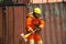 An Asian male fireman in orange protective clothing, mask and helmet with an ax standing front of building.