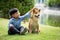 Asian male kid in blue shirt sitting touching brown Shiba inu dog in green park