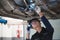 Asian male mechanical hold and shining flashlight to examine car under chassis of automotive vehicle. Safety suspension inspection