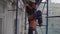 Asian male worker in orange vest and helmet goes down stairs from scaffolding