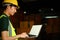 Asian male worker in safety uniform using laptop, working in warehouse full of tall shelves with goods in cardboard