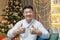 Asian man on Christmas looks into the web camera and smiles shows his fingers up affirmatively, the man sits at home on