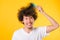 Asian man combing curly hair on yellow background