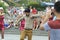 Asian man dancing on a street with cheerleaders, another man taking picture of him