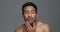 Asian man, face and skincare for grooming, hygiene or facial treatment against a grey studio background. Portrait of