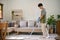 Asian man focusing on cleaning his living room, using stick vacuum cleaner to clean the carpet