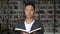 Asian man holding a blocknote standing looking straight ahead in the library