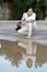 Asian man holds a big black mirrorless camera medium format type on cement asphalt ground in front of water reflex