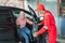 Asian man in red uniform helps open the door when a customer comes by car for repair