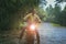 asian man riding small enduro motorcycle crossing flowing creek in forest among rain falling