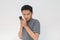 Asian man serious face and sharp looking with hiding the phone gesture  grey background