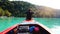 Asian man sitting on the prow of wooden boat at the turquoise sea.