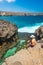 Asian man sitting on rock at Angel Billabong. A crystal clear natural tidal pool in Nusa Penida island near Bali island, Indonesia