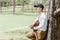 Asian man sitting and singing with guitar under pine tree