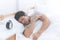 Asian man sleeping side way on white bed with alarm clock