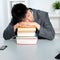 Asian man sleeping on top of a pile of books