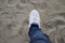 An Asian man with white shoes and blue jeans is taking a step forward with defocus sands background on the beach