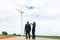 Asian man and woman Inspection engineers preparing and progress check with digital tablet of a wind turbine with safety in wind