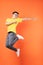 Asian man in yellow t-shirt jumping on orange background