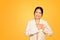 Asian millennial woman places hands on chest, expressing sincere gratitude, orange studio backdrop