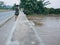 Asian mother carrying her little daughter standing on a bridge showing her little baby a murky muddy river aft