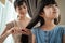 Asian mother combing little kid daughter`s hair with hairbrush at home. Beautiful loving parent mom dress up young girl child wit