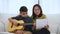 Asian mother embraces son, Asian boy playing guitar and mother embrace on the sofa and feel appreciated and encouraged. Concept of