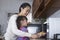 Asian mother with her little daughter using microwave oven to warm croissants in the kitchen at home