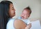 Asian mother holding screaming newborn baby boy on hands looking at him with love at bedroom