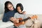 Asian mother teaches her daughter to play ukulele while sitting on the sofa in her home living room