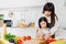 Asian Mother teaching her little child using knife to slice apple for cook food in the kitchen