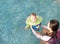 Asian Mother training for infant baby boy in swimming suit floating in pool with safety by baby neck floats