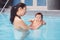 Asian mother training teaching her newborn baby to float in swimming pool.