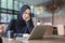 Asian muslim in black headscarf woman working with laptop in cafe.