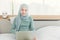 Asian Muslim Islamic woman with hijab happy enjoy online remote work at home with her laptop on the bed