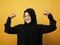 Asian muslim lady wearing hijab shows strong muscle power gesture, inner power leadership concept against yellow background