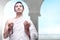 Asian Muslim man in ihram clothes standing and praying with prayer beads while raised arms