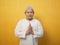 Asian muslim man smiling and shows greeting gesture against yellow background, concept of islamic celebration of ramadan or eid