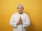 Asian muslim man smiling and shows greeting gesture against yellow background, concept of islamic celebration of ramadan or eid