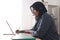 Asian muslim woman having video teleconference on her laptop at home, online learning or working from home