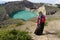 An Asian Muslim woman wearing a hijab is taking a photo in front of a green view of the Kelimutu-Flores lake