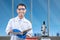 Asian nerd scientist standing and holding a book with a microscope and medical tube rack on the desk