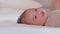 An Asian newborn baby is laying down on a soft white sheet mattress. Starring at his parents and feels sleepy. Adorable chubby boy