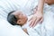 Asian newborn baby is sleeping on white bed with mother hand put on her chest to take care and make her feel safe