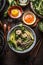 Asian noodles bowl with green vegetables, bok choy and meat balls on dark background with wooden cutlery, chopsticks and hot sauce