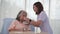 Asian nurse feeding breakfast to elderly female patient on bed in hospital ward