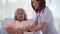 Asian nurse helping elderly woman patient to drink on bed at hospital ward